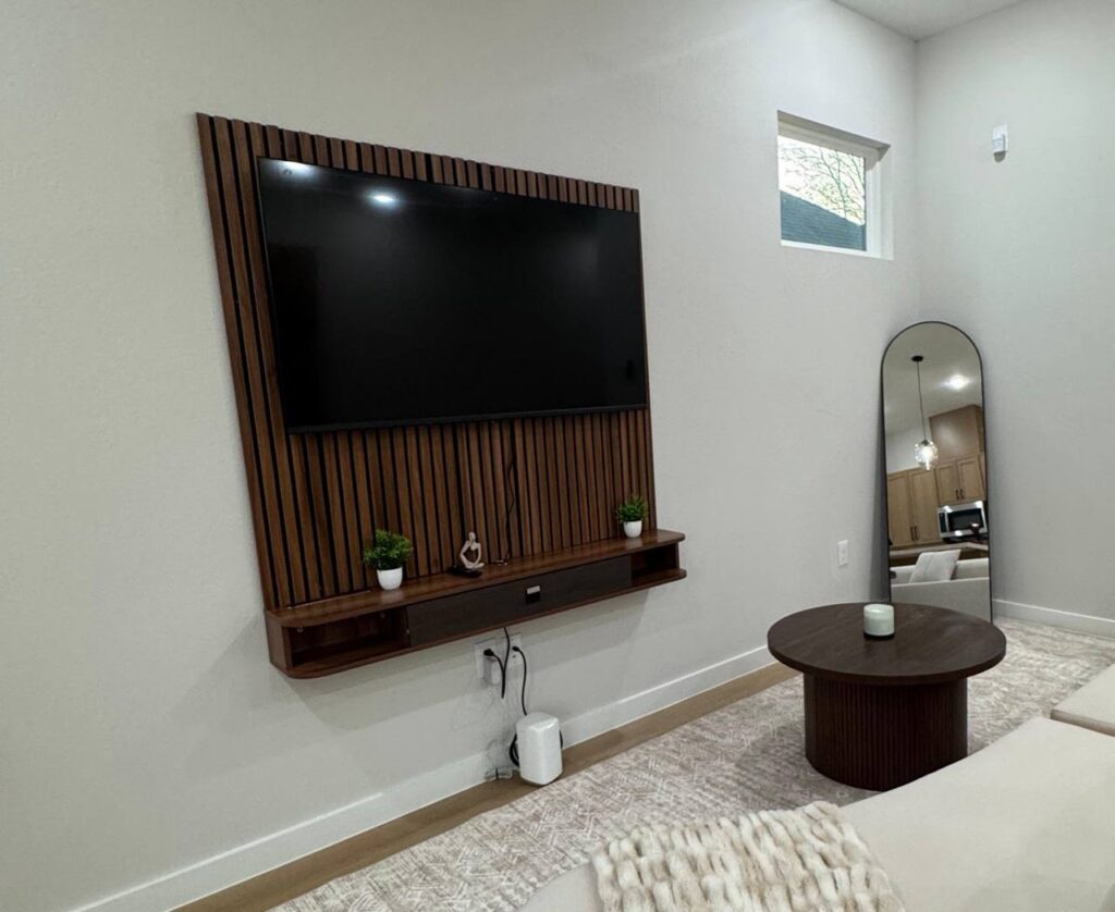 Modern marble accent wall TV mounting with green chairs in a premium Houston living room